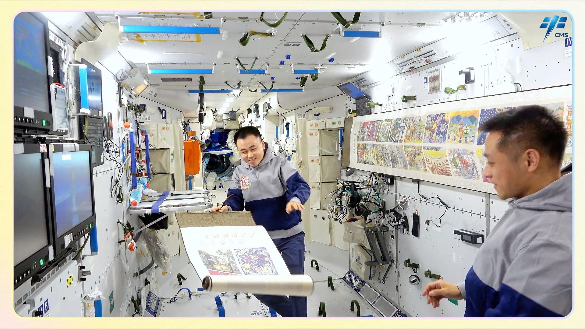 Tang Shengje (left) and Jiang Xinlin (right) aboard the Tiangong Space Station unrolling artwork for display during the Shenzhou 17 mission. ©China Manned Space Agency